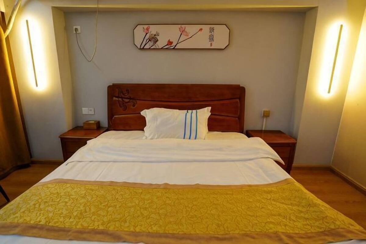 A hotel room with a large bed, wooden headboard, bedside tables, and a wall-mounted artwork.