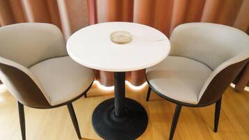 A round table with a glass top, flanked by two chairs with dark legs and light-colored upholstery.