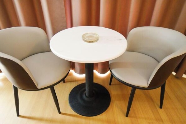 Una mesa redonda con superficie de vidrio, acompañada por dos sillas con patas oscuras y tapicería clara.