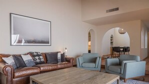 A living room with a brown leather sofa, a wooden coffee table, and two light blue armchairs. There is a dining area with a table and chairs in the background. - Spacious Arcadia Lite house w/ pool, mtn. views (Phoenix)