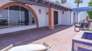 A covered patio area with a brick floor, a table and chairs, and a pool area with tiled walls. - Spacious Arcadia Lite house w/ pool, mtn. views (Phoenix)