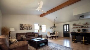 A spacious living room with a large brown leather sofa, a coffee table, and a dining area with a chandelier. - Urban Edge | Comfort & Fun: Large Game Room & Fitness Room (Decorah)