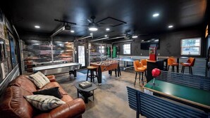 A cozy indoor space with a foosball table, a sofa, and a bar area with stools. - Urban Edge | Comfort & Fun: Large Game Room & Fitness Room (Decorah)