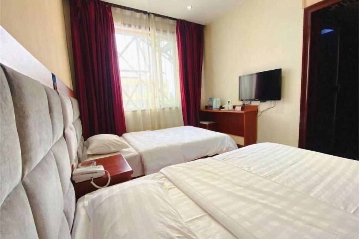 Ein Hotelzimmer mit zwei Betten, einem Fernseher und einem Fenster mit Vorhängen.