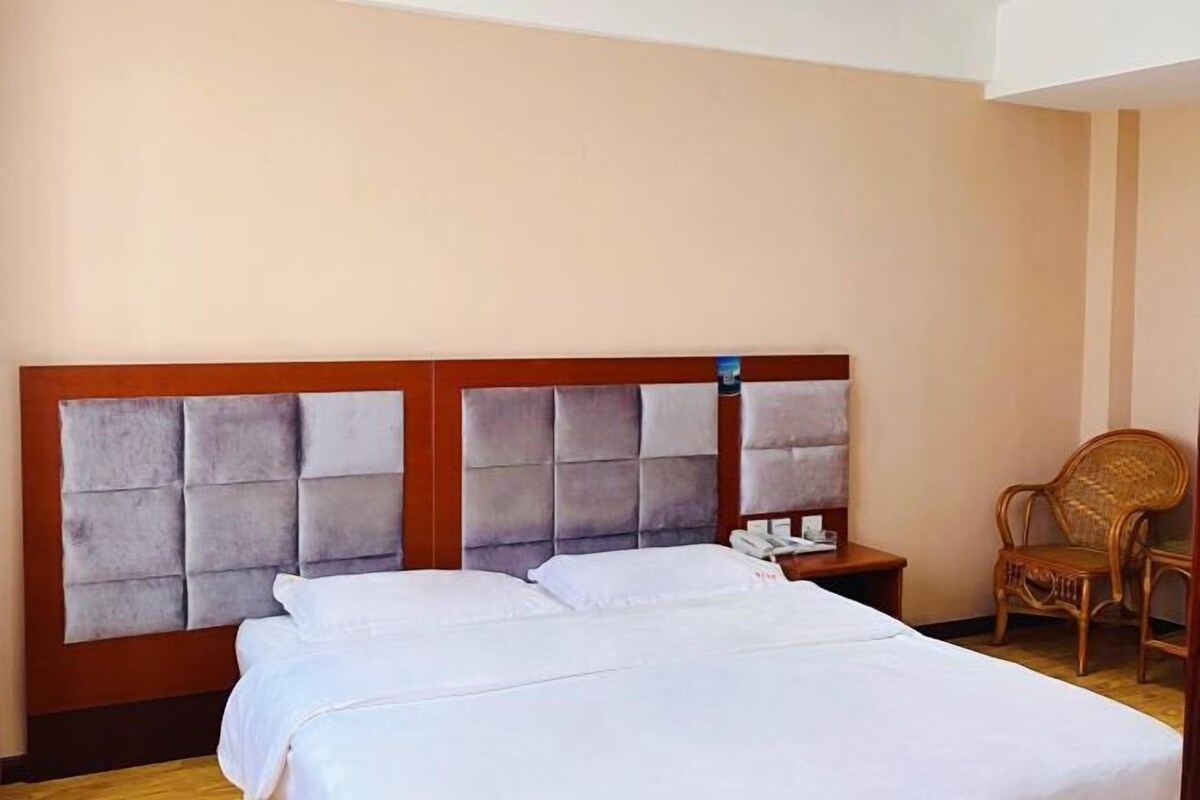 A hotel room with a large bed, a wooden headboard, a bedside table with a phone, and a wicker chair.