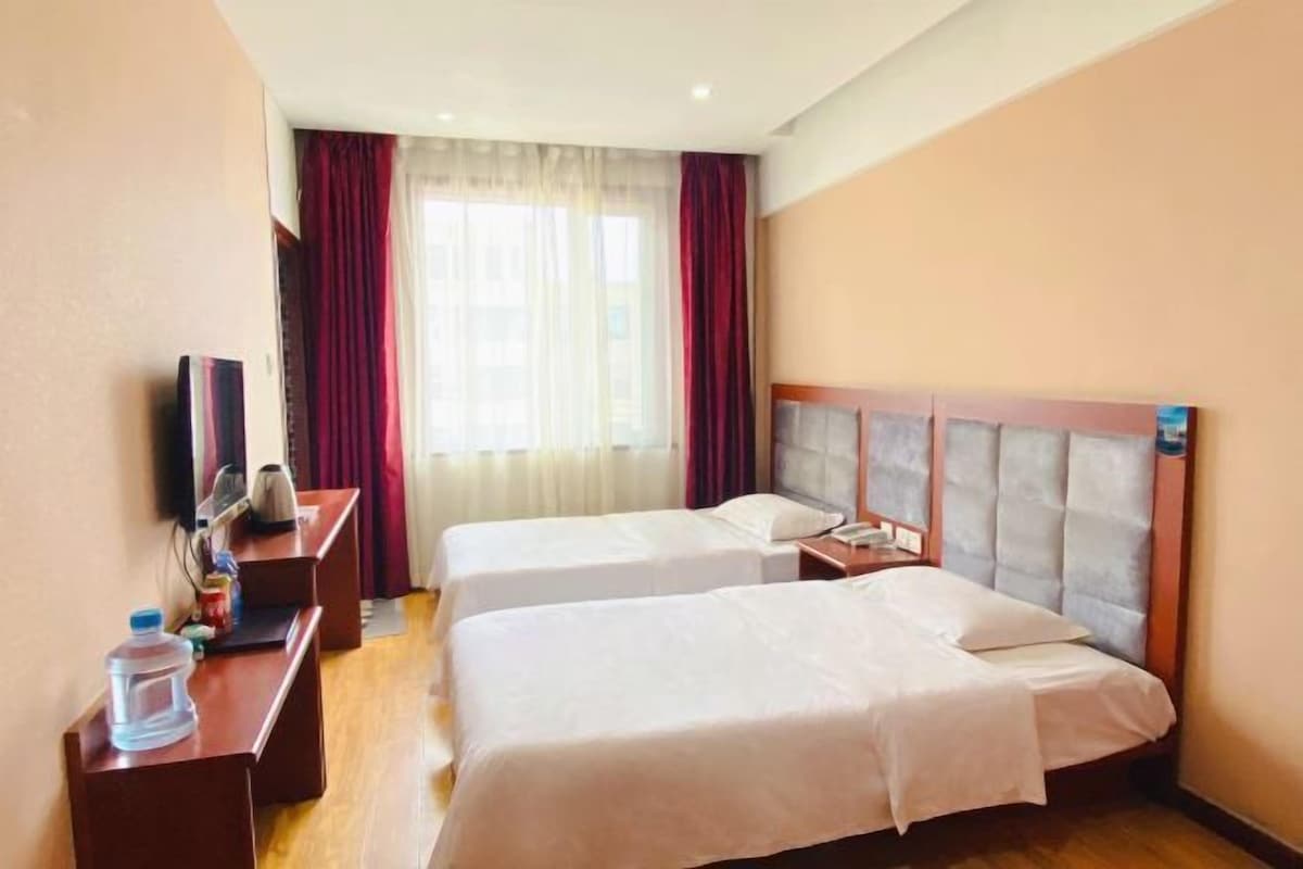 A hotel room with two beds, a desk with a chair, a television, and a window with curtains.
