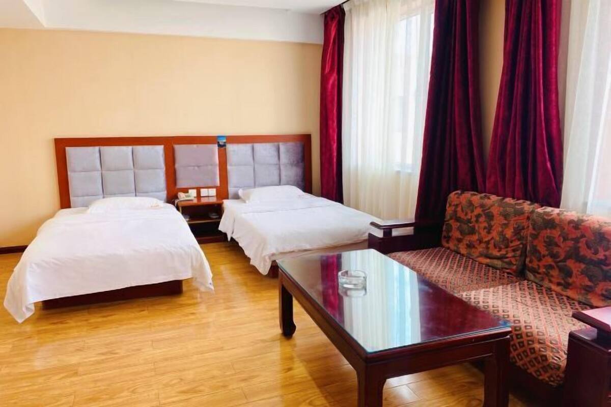 Ein Hotelzimmer mit zwei Betten, einem Schlafsofa, einem Glastisch und einem Nachttisch mit Lampe.
