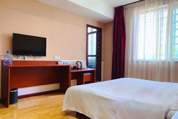 A hotel room with a bed, a desk, a television, and a window with curtains. - Yaqi Hotel (Pingdu)