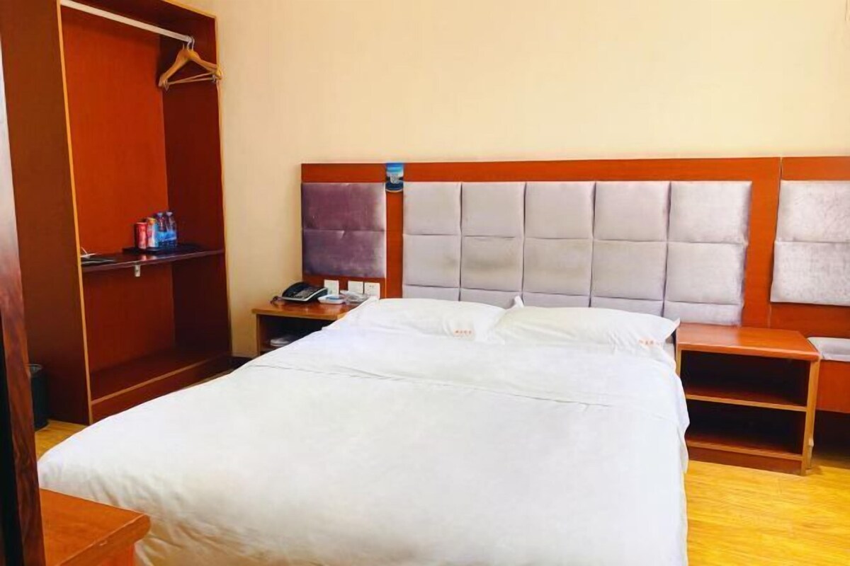 A hotel room with a large bed, wooden headboard, a wardrobe, and a bedside table with a lamp.