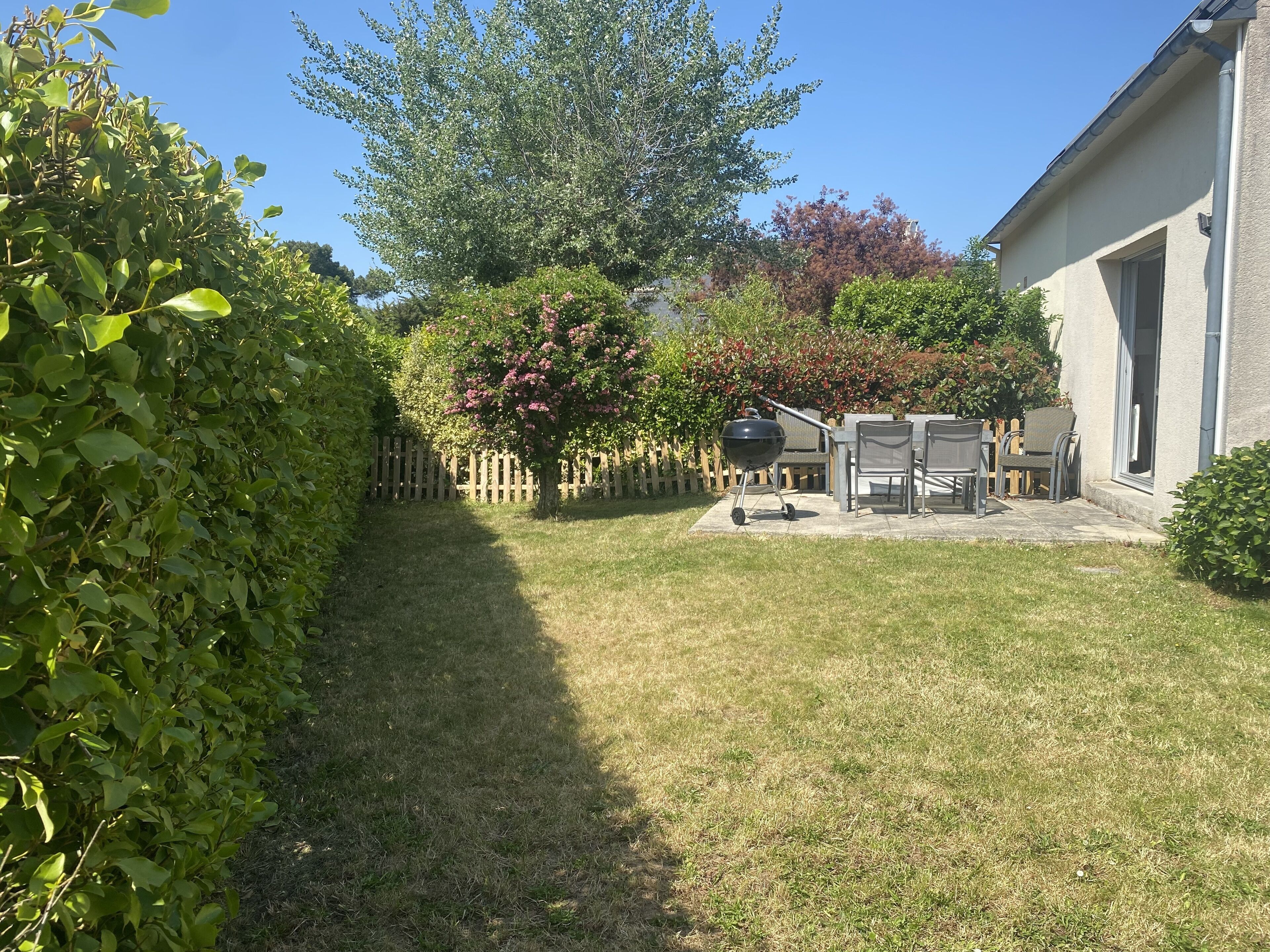 Un patio trasero con zona de barbacoa, cercado de madera y una casa.