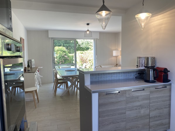 A modern kitchen with a dining area, large windows, and a coffee maker.