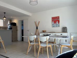 Uma cozinha moderna com armários brancos, uma área de jantar com cadeiras brancas, uma mesa de jantar de madeira e um lustre.