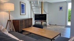 Una sala de estar moderna con sofá, mesa de centro, televisor sobre un mueble, lámpara y una escalera que conduce a un nivel superior.