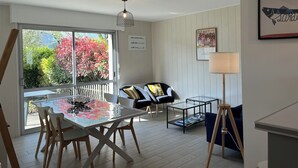Un comedor con una mesa de vidrio, sillas, una lámpara y vistas a árboles por una ventana.
