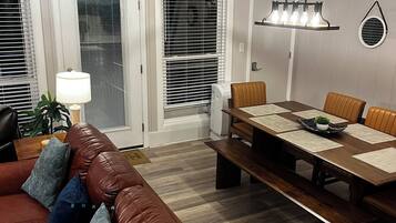 A living room with a brown leather sofa, a dining table with chairs, and a ceiling light fixture.