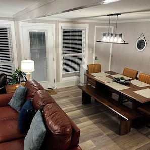 A living room with a brown leather sofa, a dining table with chairs, and a ceiling light fixture. - Beech Mountain Townhome 3/2, Heated pool, Hot tub, hiking, 0.5 mil to Ski slopes (Beech Mountain)