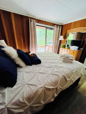 A hotel room with a bed, a dresser, a television, and a window with curtains.