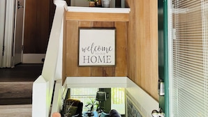 Een houten interieur met een bordje 'welkom in ons huis', een trap, een bank en een lamp.