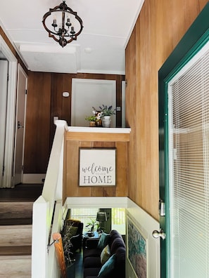 A wooden interior with a 'welcome to our home' sign, a staircase, a sofa, and a lamp.