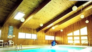 Een binnenzwembad met houten wanden en plafond, grote ramen en een blauw zwembad.