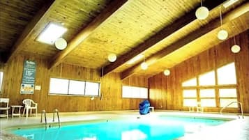 An indoor swimming pool with wooden walls and ceiling, large windows, and a blue pool.