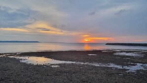 Ein Kiesstrand mit Sonnenuntergang über dem Wasser.