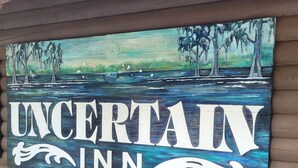 Une enseigne murale pour « UNCERTAIN INN », représentant un paysage peint avec des arbres et de l’eau.