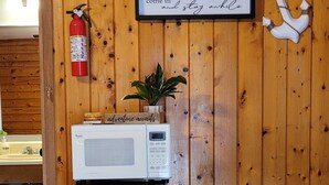 Une cuisine compacte avec un mur en bois, un réfrigérateur noir, un four à micro-ondes blanc et une petite table.