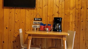 Un mur lambrissé en bois, un tableau noir, une machine à café et une table avec des chaises.