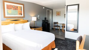 A hotel room with a large bed, a desk with a chair, a coffee machine, and a framed picture on the wall.