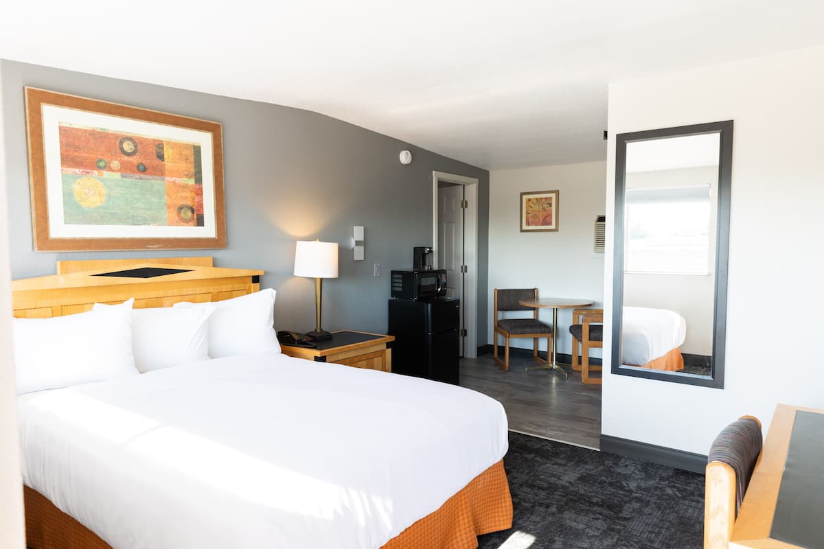 Ein Hotelzimmer mit einem großen Bett, einem Schreibtisch mit Stuhl, einer Kaffeemaschine und einem gerahmten Bild an der Wand.