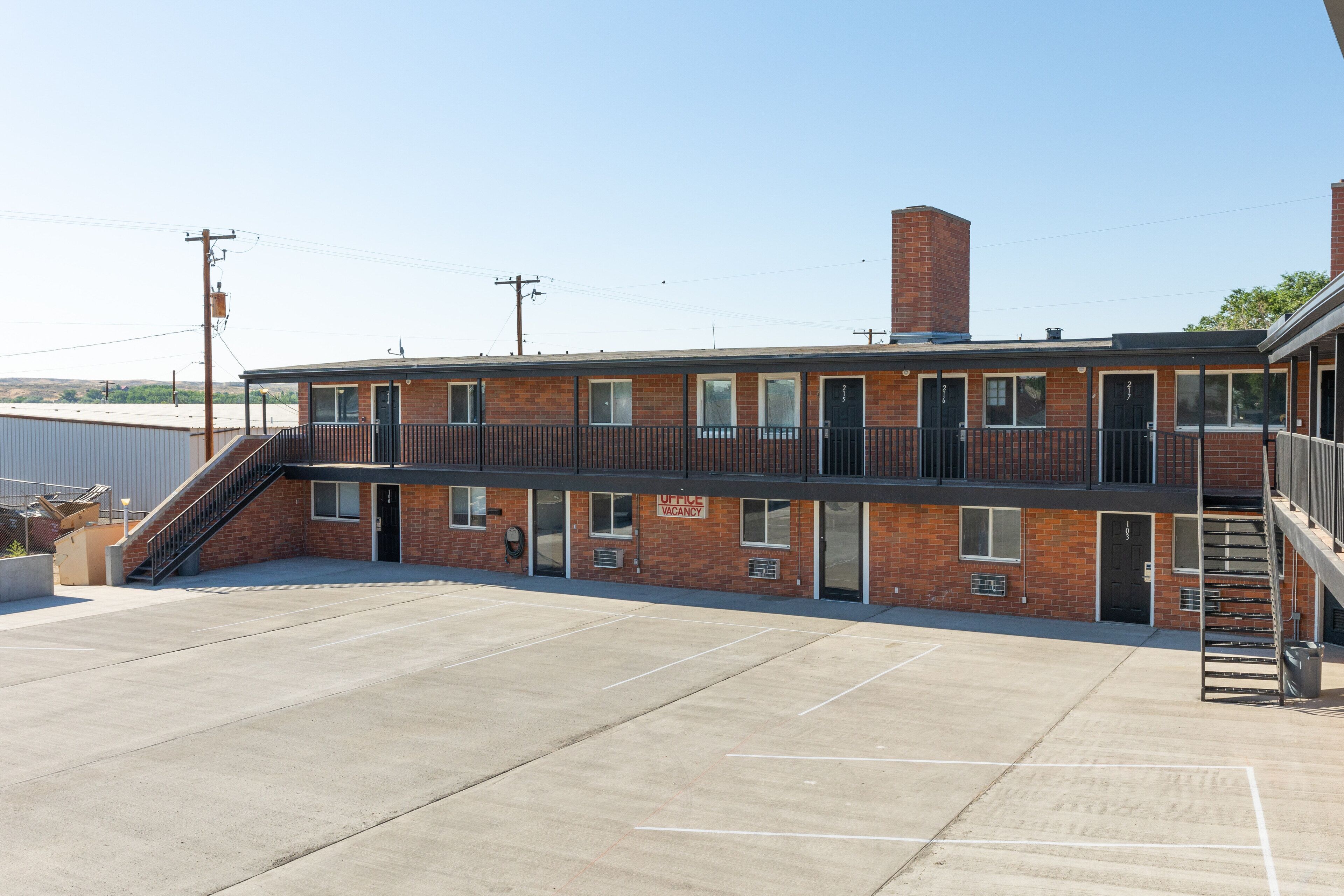 A two-story building with a brick facade, a covered parking area, and a sign indicating an office vacancy.