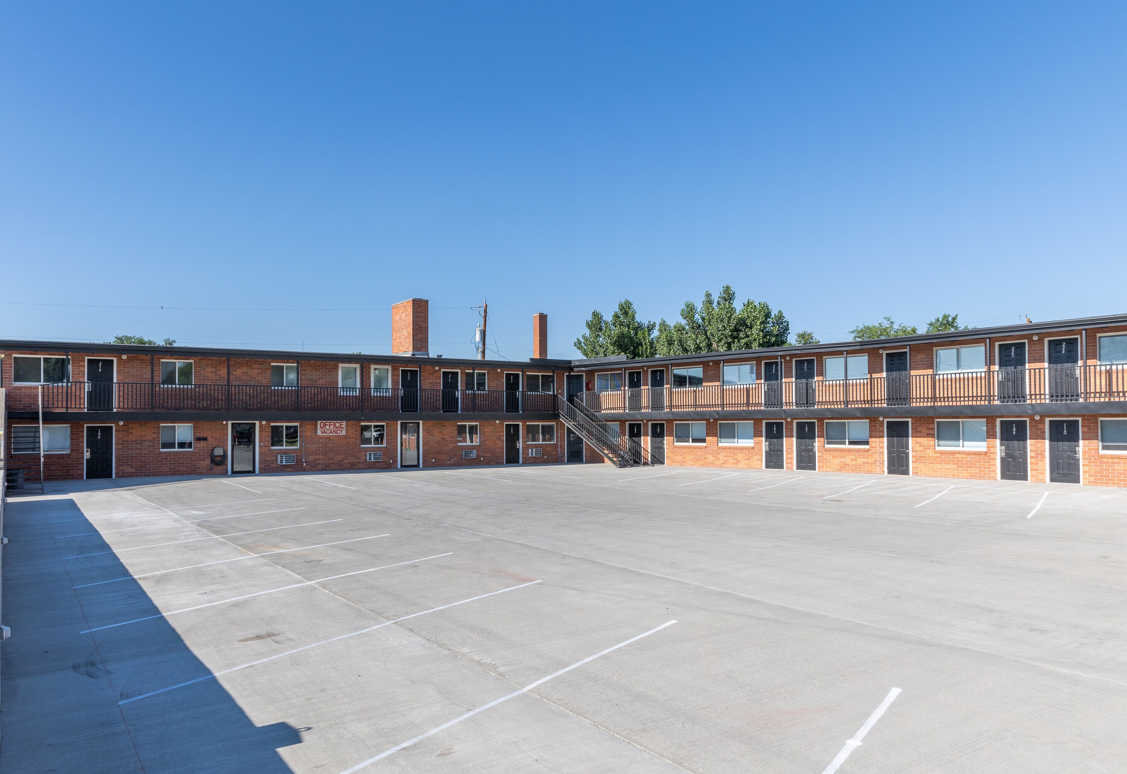 A multi-story brick building with a central staircase, a parking lot, and a clear blue sky.