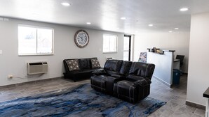 A spacious living area with a black leather sofa, a blue patterned rug, and a wall clock.