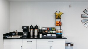 A kitchen with a coffee station, a fruit basket, and a trash can.