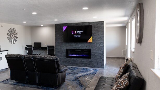 A modern living room with a black leather sofa, a black leather couch, a flat-screen TV mounted on a stone wall, and a fireplace.