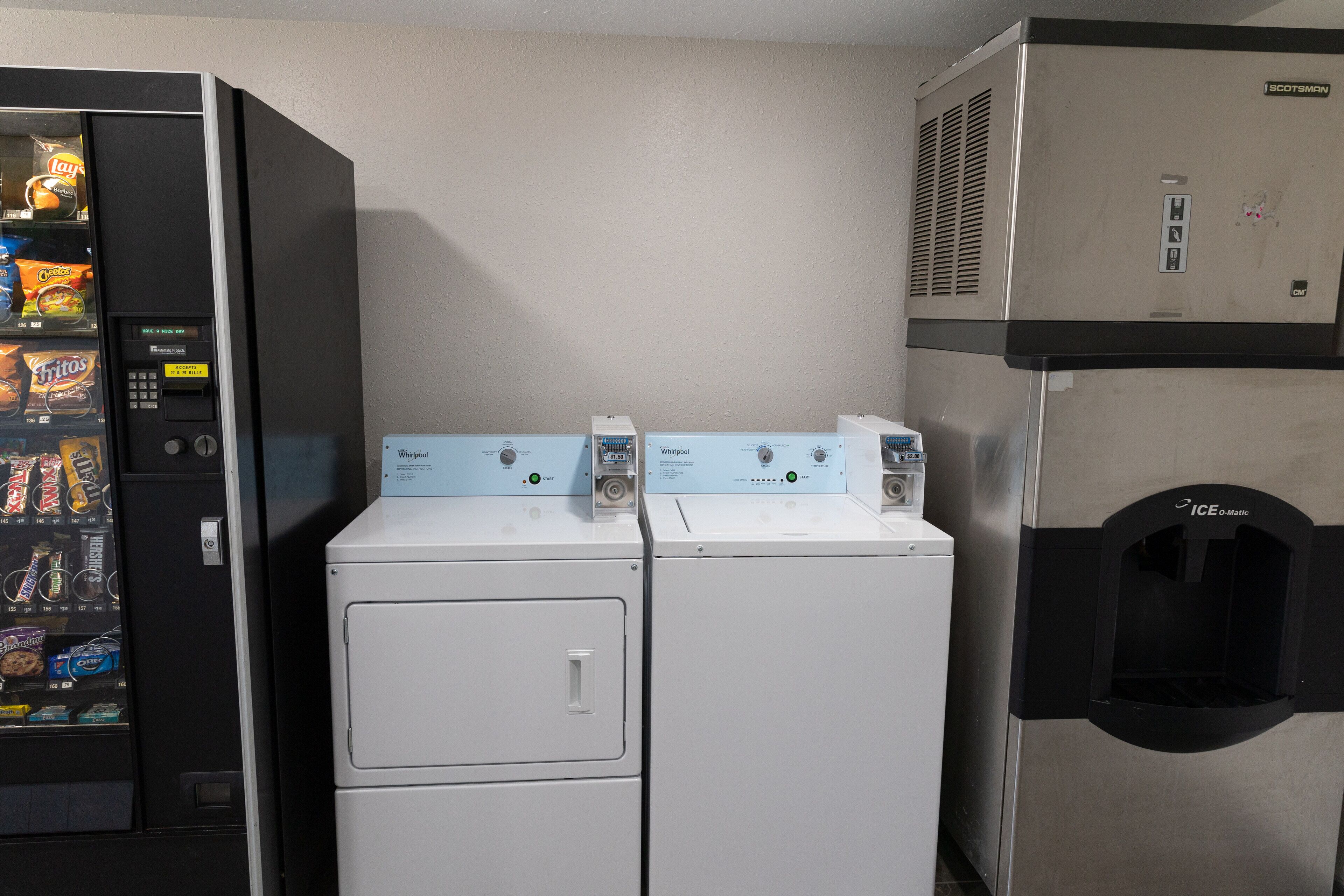 A laundry area with a vending machine, two washers, and a refrigerator.