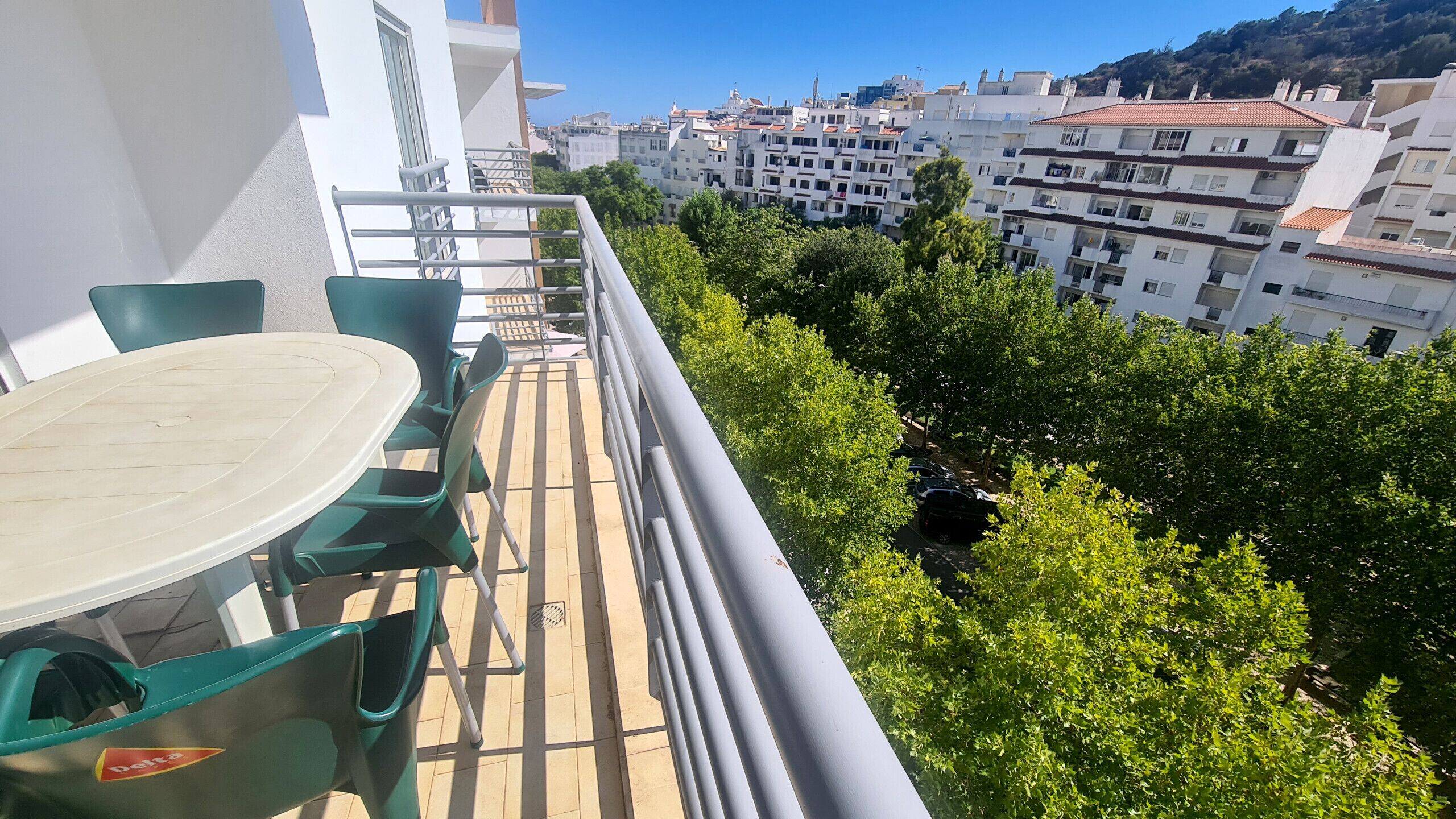 Un balcon avec une table et des chaises, donnant sur un paysage urbain composé d’immeubles et d’arbres.