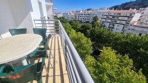 En balkong med ett bord och stolar, med utsikt över en stadsmiljö med byggnader och träd.