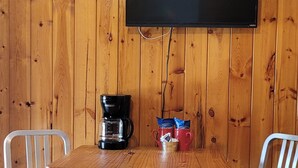 A wooden-paneled room with a table, two chairs, a coffee maker, a mug, and a flat-screen TV mounted on the wall. - #15 Off the Hook-Uncertain Lodge and Inn (Karnack)