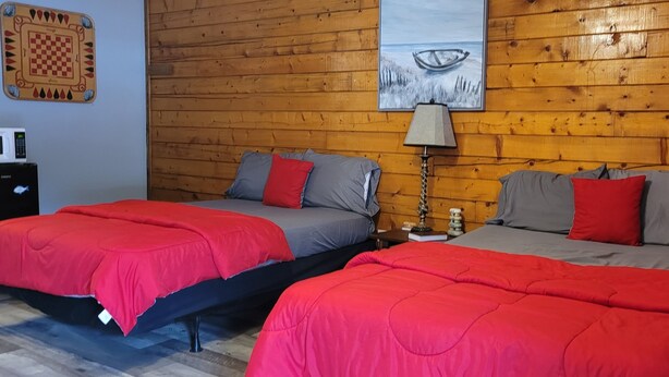 Two beds with red and grey bedding, a wooden wall, a lamp, and a checkered board game. - #15 Off the Hook-Uncertain Lodge and Inn (Karnack)