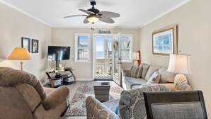 Ein Wohnzimmer mit Deckenventilator, Fernseher, Sofa, Couchtisch und einer Tür zum Balkon.