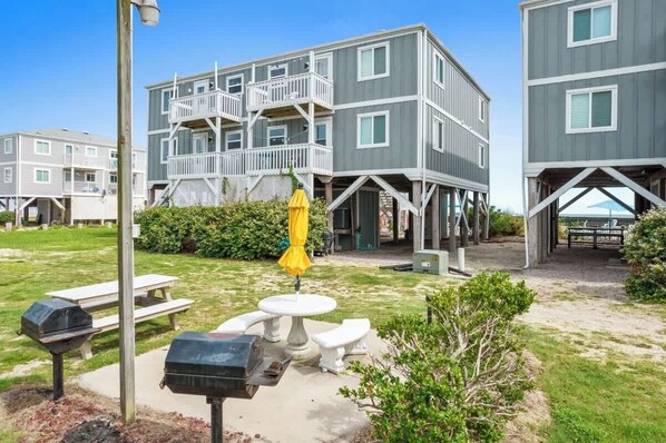 A multi-story building with balconies, a patio area with a table and chairs, and a barbecue grill.