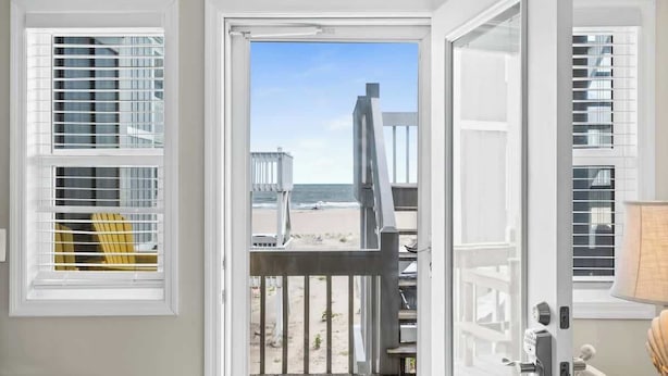 Eine Tür mit Blick auf einen Strand, eine Holzterrasse und ein Stuhl.