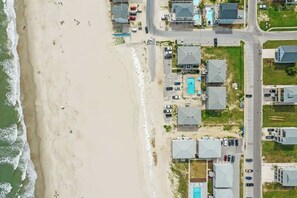 An aerial view of a coastal residential area with houses, a beach, and a road.