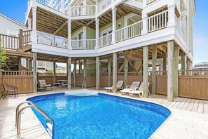 A multi-level outdoor swimming pool area with wooden deck, lounge chairs, and a covered deck.