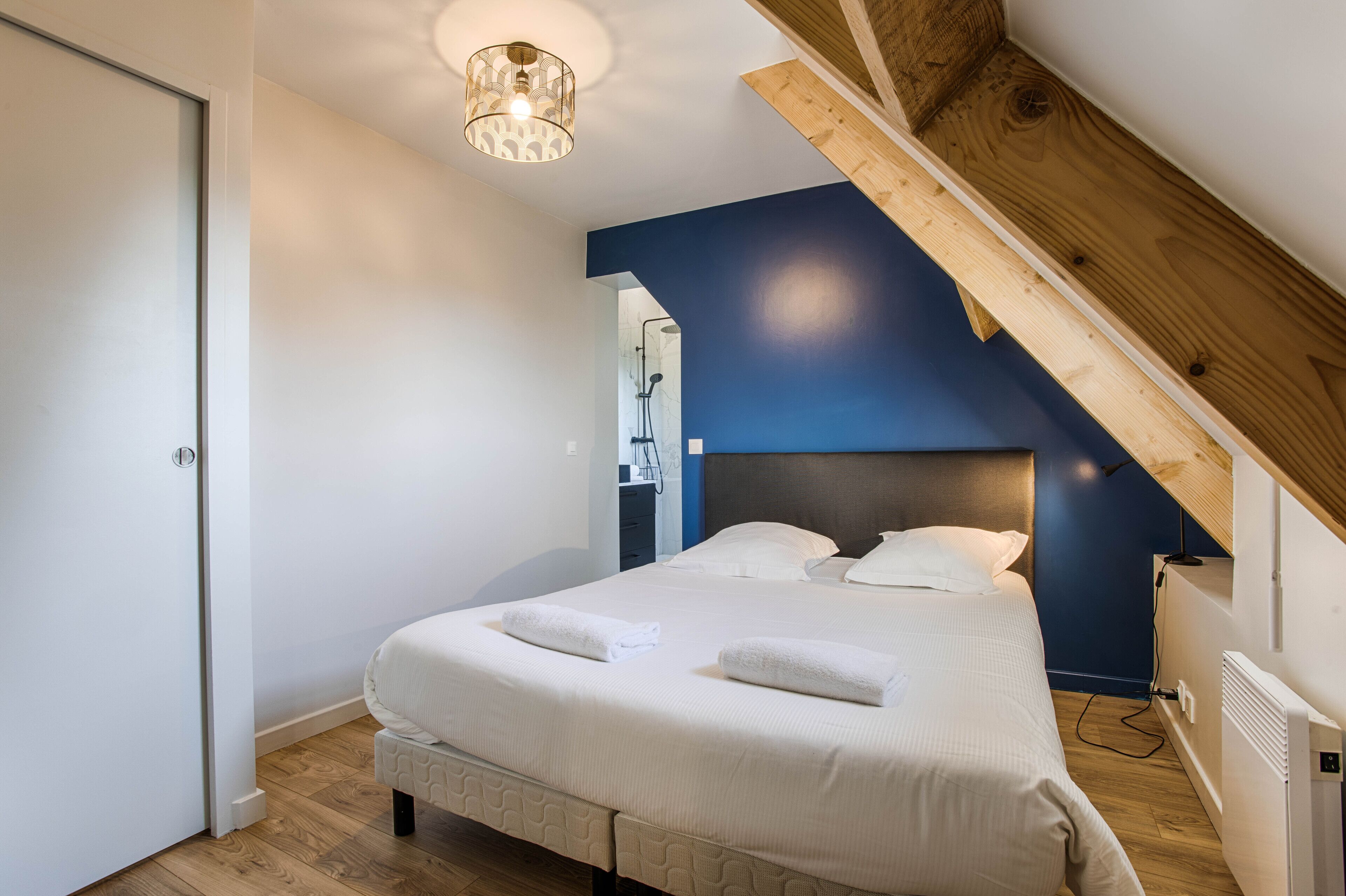 Ein Schlafzimmer mit einem Bett, weißer Bettwäsche, einer Holzbalkendecke und einem weißen Heizkörper.