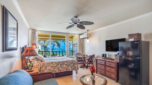 A hotel room with a bed, a sofa, a dining area, a refrigerator, and a television. - Ocean View Beachfront, Split AC Wifi, Pool Hot Tub (Kapaa)