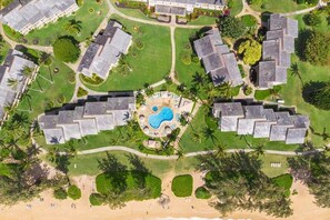 An aerial view of a resort with multiple buildings, a central pool area, and surrounding greenery. - Ocean View Beachfront, Split AC Wifi, Pool Hot Tub (Kapaa)