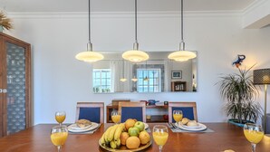 Et spiseområde med et træbord dækket til morgenmad, inklusive frugtfat, croissanter og appelsinjuice.